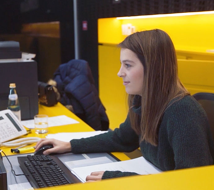 TechnoAlpin Mitarbeiterin am Arbeitsplatz im modernen Büro mit gelber Wandgestaltung