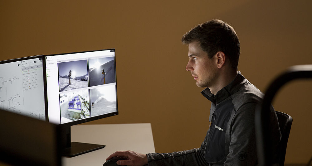 TechnoAlpin Mitarbeiter überwacht Beschneiungsanlage über Monitore mit Kameraansichten