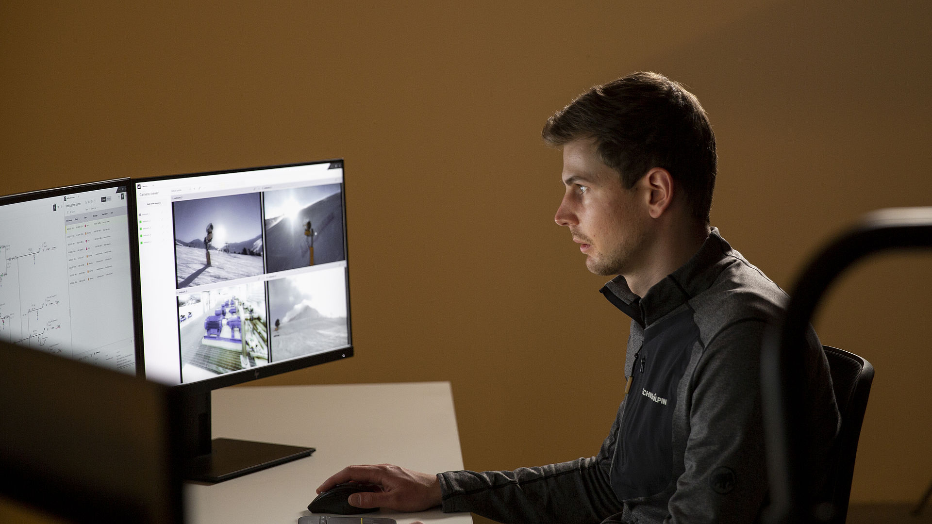 Collaborateur TechnoAlpin dans un bureau sombre surveille les écrans du système d'enneigement avec les caméras en direct des canons à neige