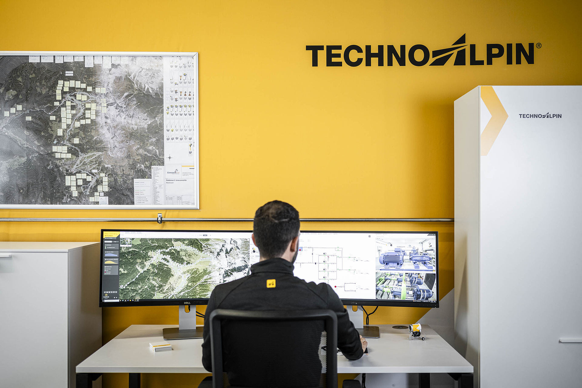 TechnoAlpin Kontrollraum mit Mitarbeiter vor Doppelmonitor und Steuerschrank für Beschneiungssysteme