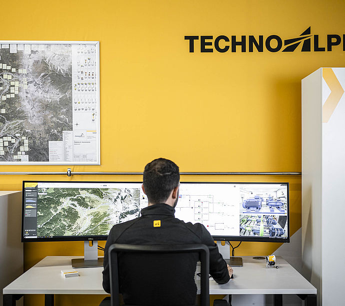TechnoAlpin Kontrollraum mit Mitarbeiter vor Doppelmonitor und Steuerschrank für Beschneiungssysteme