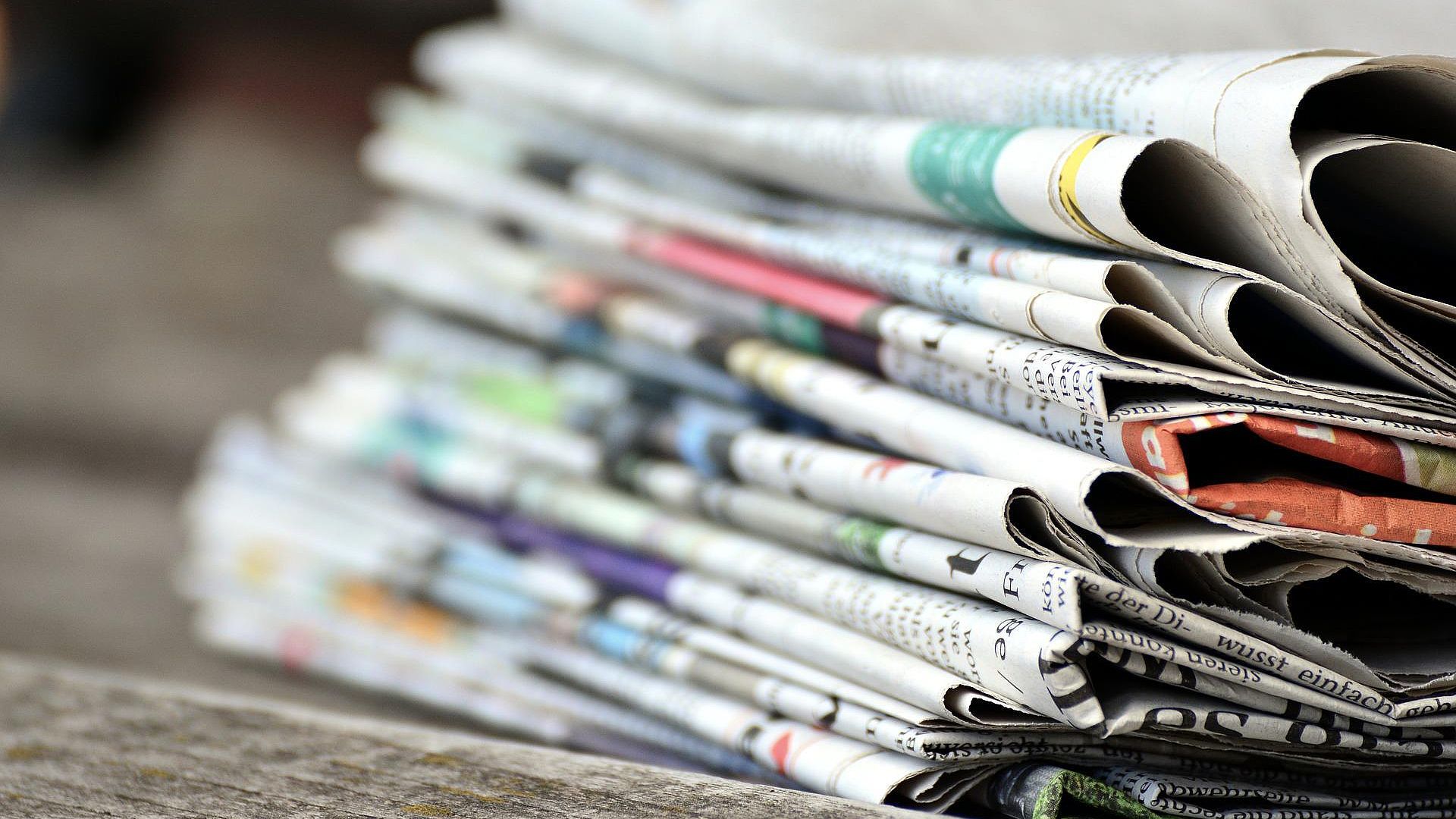 Stapel gefalteter Zeitungen auf Holzoberfläche als Symbol für Pressemitteilungen und Medienberichterstattung