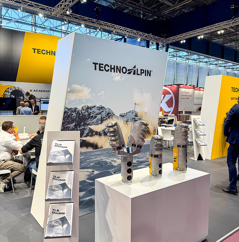 TechnoAlpin Markenwand mit Bergmotiv und drei TL8 Schneeerzeuger-Düsenköpfen auf weißem Podest