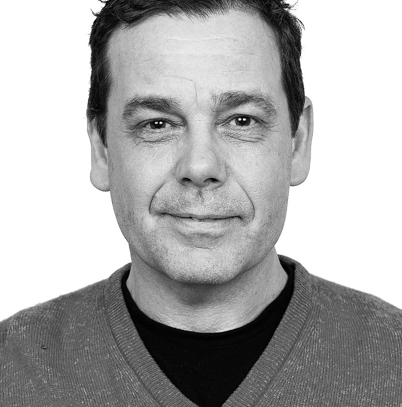 Lars Westblad, TechnoAlpin Nordic Mitarbeiter, Schwarz-Weiß-Portrait mit kurzem dunklem Haar und dezentem Lächeln in grauem V-Ausschnitt-Pullover
