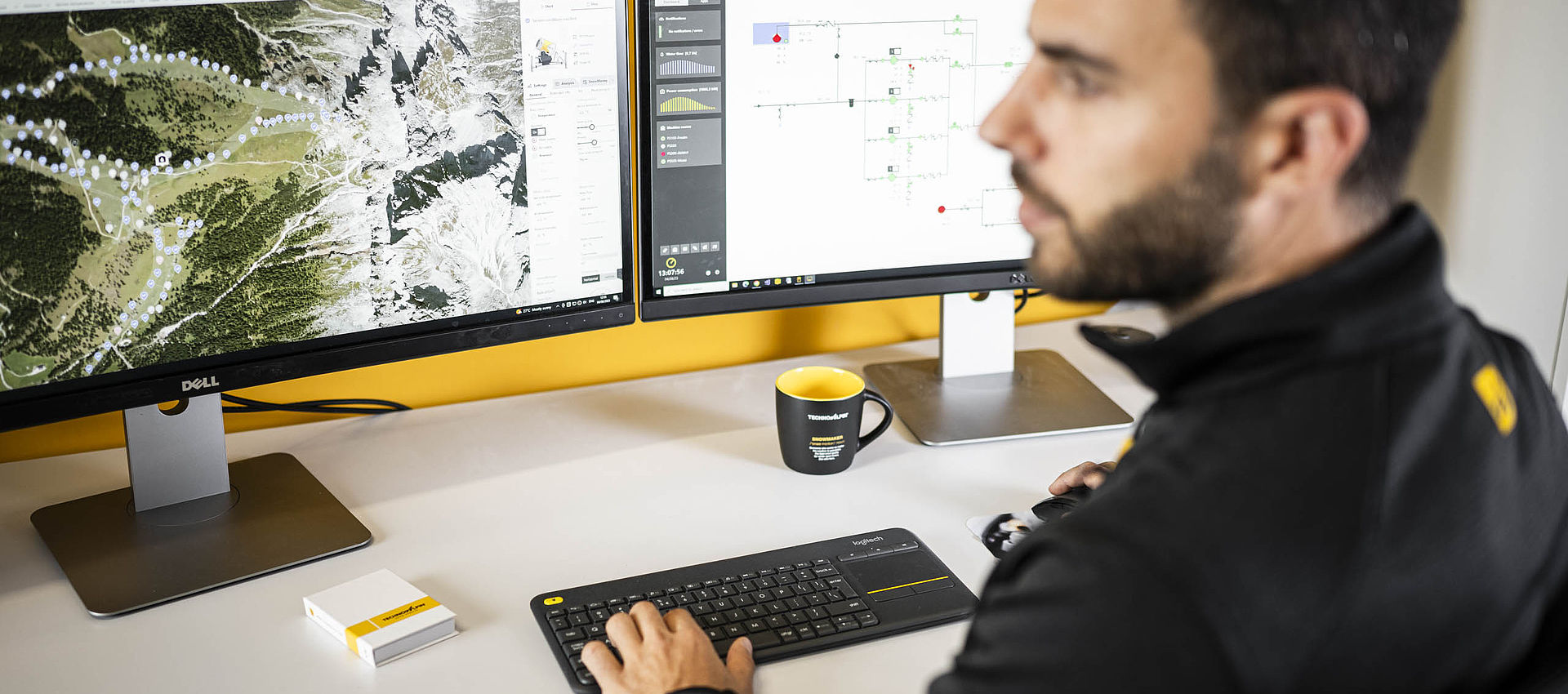 TechnoAlpin Techniker arbeitet am Doppelmonitor mit Skigebiets-Karte und Steuerungssoftware