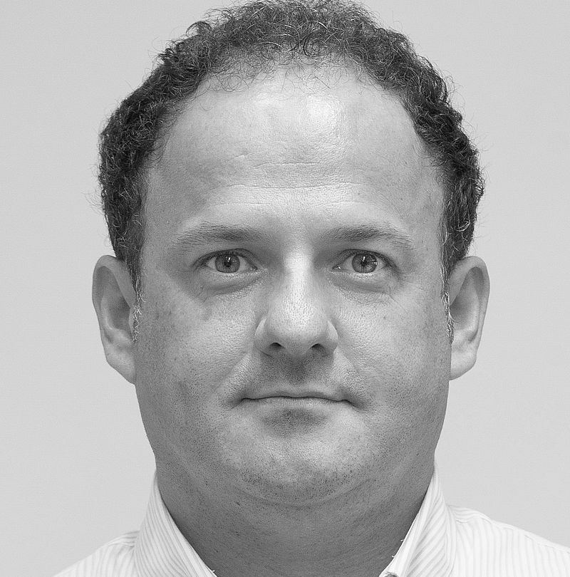 Federico Zanardini, TechnoAlpin Mitarbeiter, Schwarz-Weiß-Portrait mit lockigem dunklem Haar, rasiert und neutralem Ausdruck in weißem Nadelstreifenhemd
