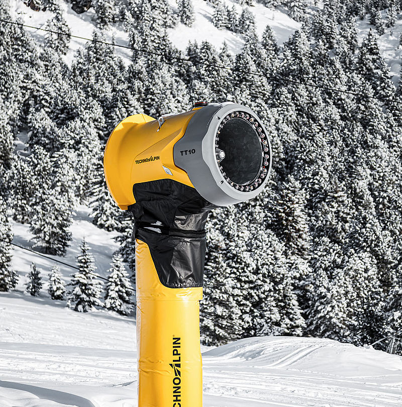Side view of the TechnoAlpin TT10 snow gun in front of snow-covered mountain forest