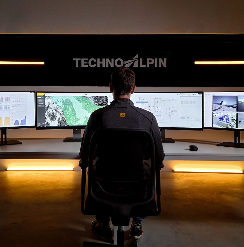 TechnoAlpin Leitstand mit Mitarbeiter und Multi-Monitor-Setup zur Beschneiungssteuerung