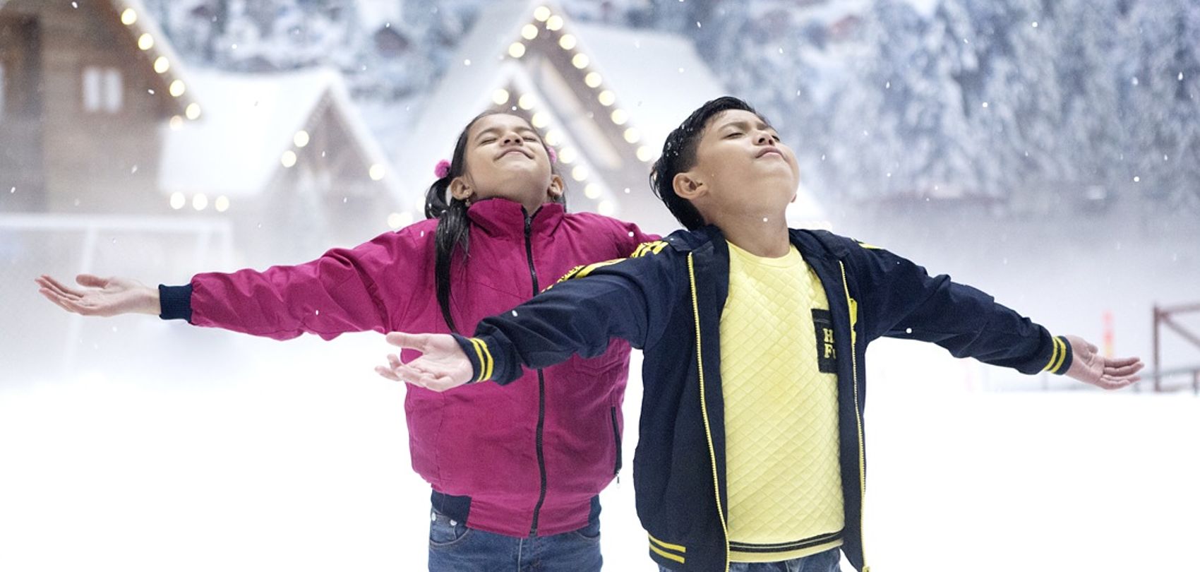 Two children with outstretched arms enjoy snow in indoor snow hall