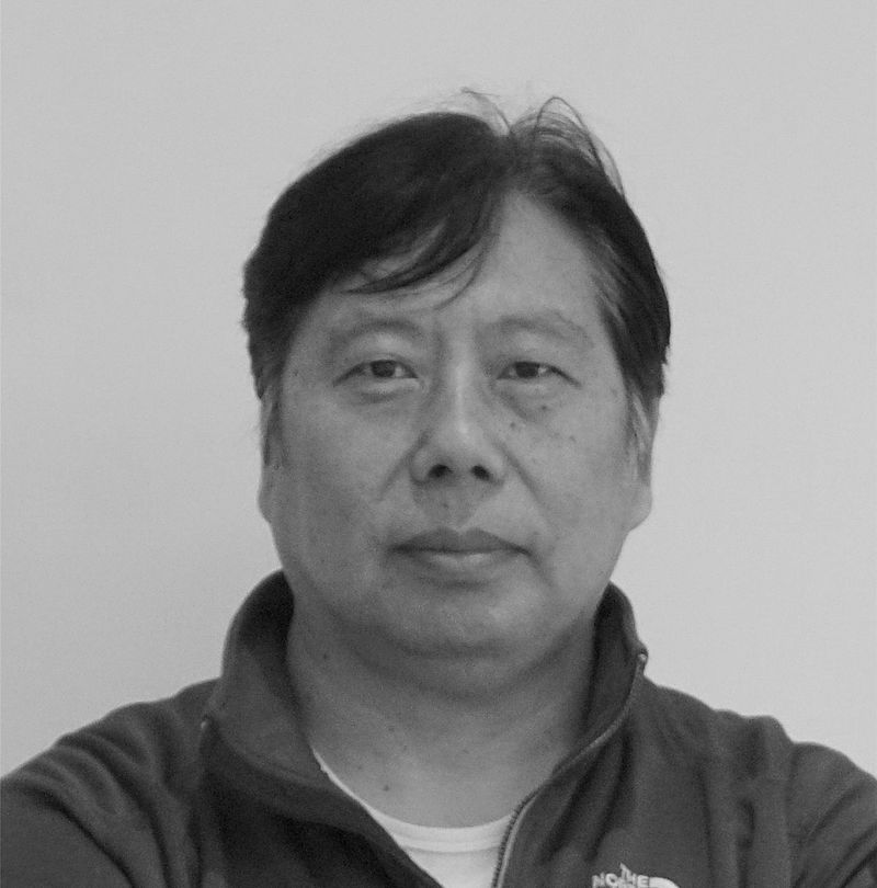 Shengming Lue, TechnoAlpin Mitarbeiter, Schwarz-Weiß-Portrait mit North Face Jacke und neutralem Ausdruck vor hellem Studiohintergrund