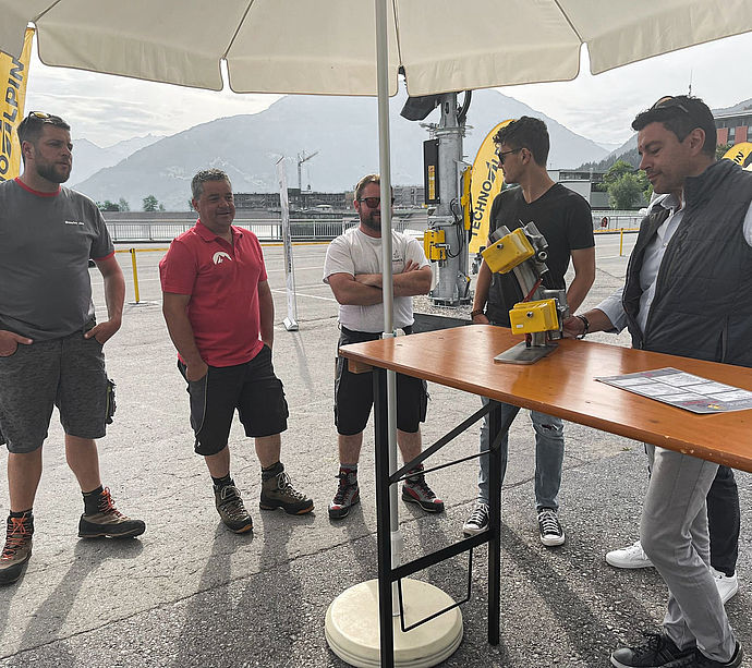 Technical consultation under parasol with TechnoAlpin employee and ski resort operators.