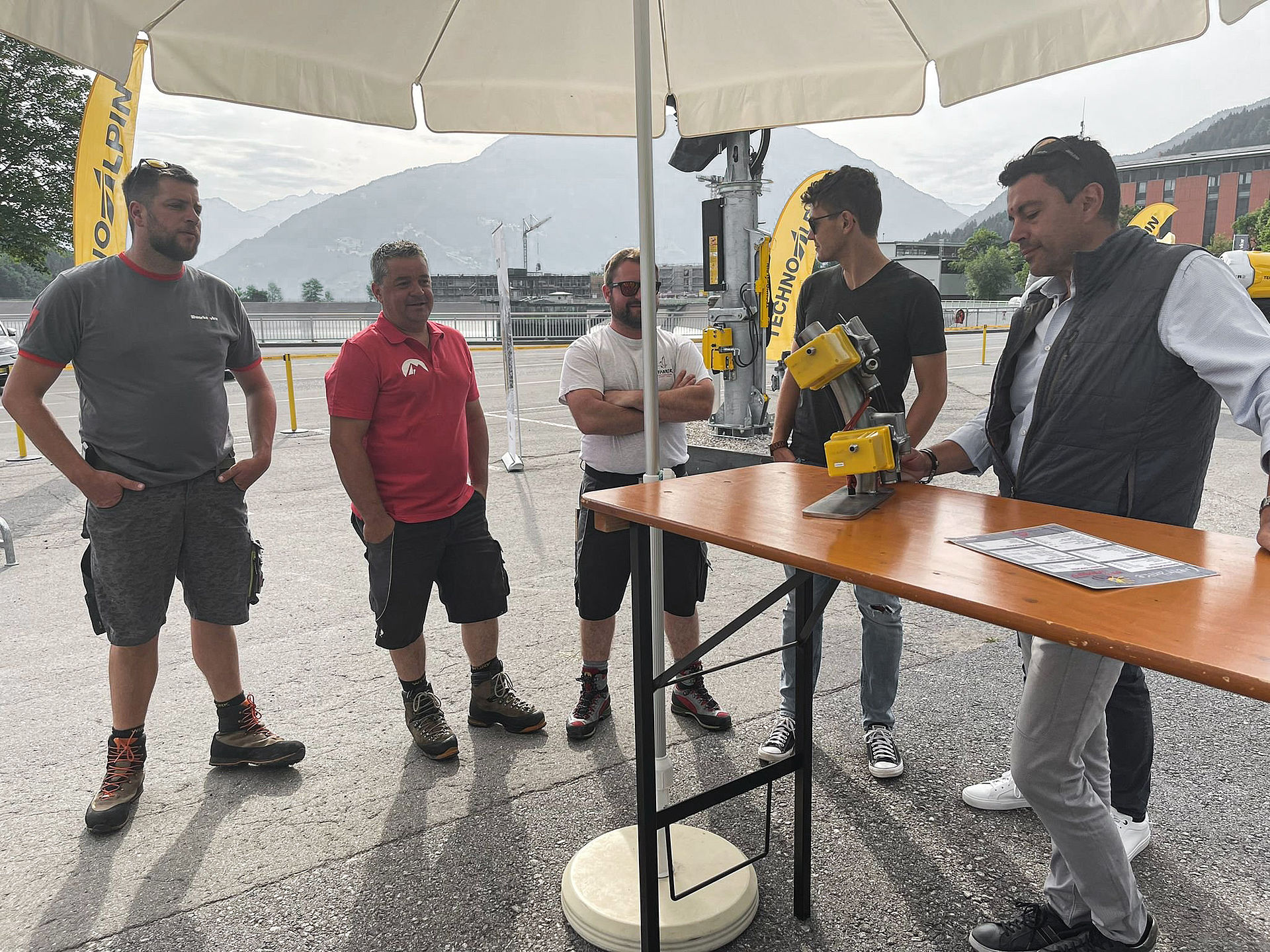 Technical consultation under parasol with TechnoAlpin employee and ski resort operators.