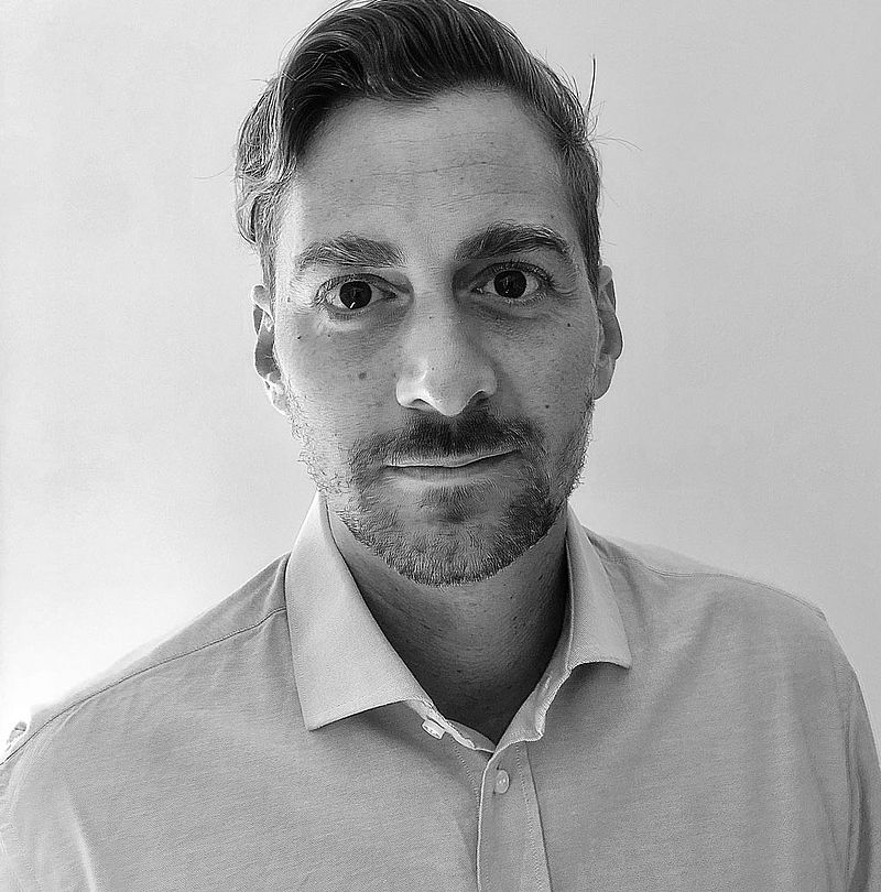 Alessio Di Girolamo, TechnoAlpin Mitarbeiter, Schwarz-Weiß-Portrait mit dunklem zurückgekämmtem Haar, kurzem Bart und neutralem Ausdruck in hellem Hemd