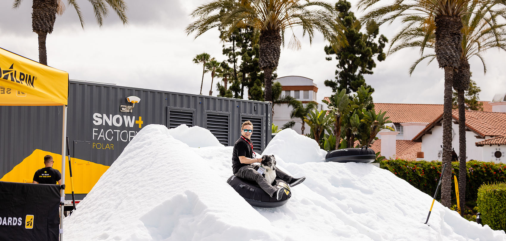 Homme sur snowtube sur tas de neige blanc avec palmiers et container SnowFactory