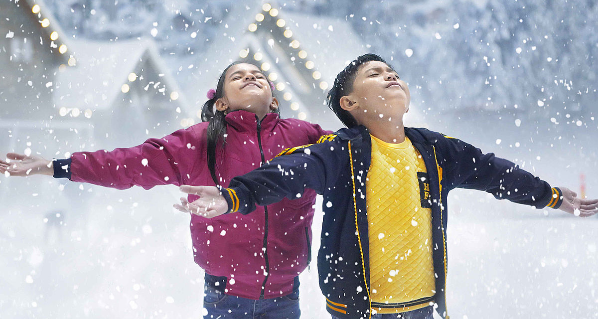 Kinder strecken die Arme im fallenden Indoor-Schnee einer TechnoAlpin SNOWSKY Anlage aus