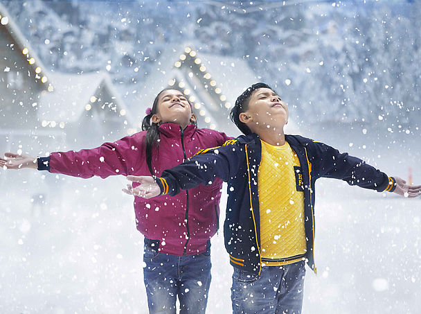 Kinder strecken die Arme im fallenden Indoor-Schnee einer TechnoAlpin SNOWSKY Anlage aus