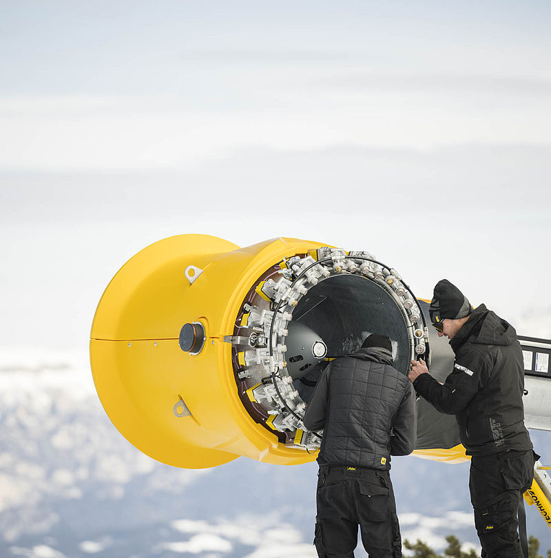 Zwei TechnoAlpin Techniker warten geöffnete gelbe Schneekanone auf verschneitem Bergkamm