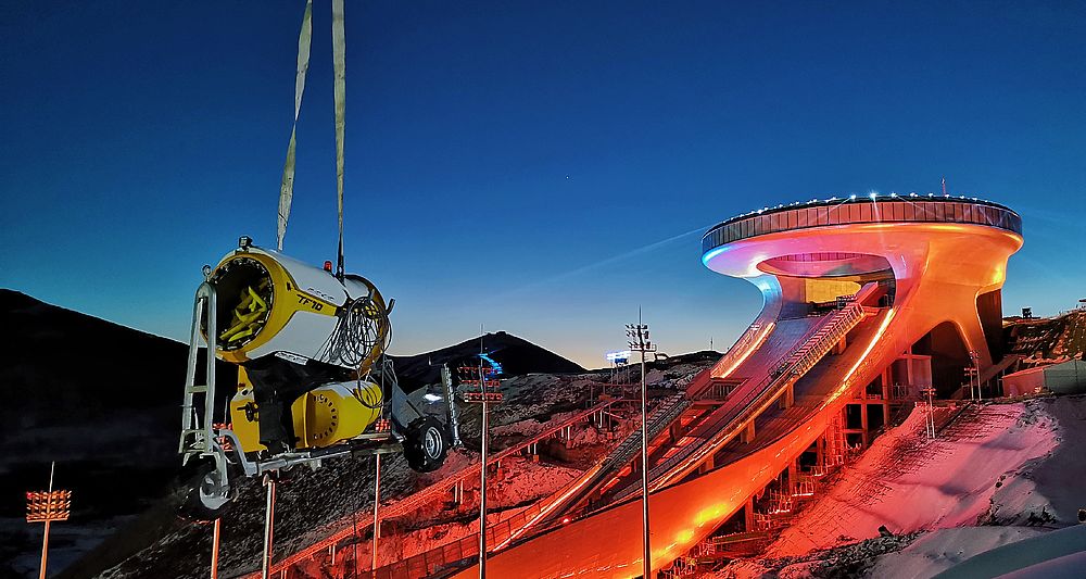 Generatore di neve TF10 giallo sospeso da gru al Big Air Shougang di Pechino al crepuscolo