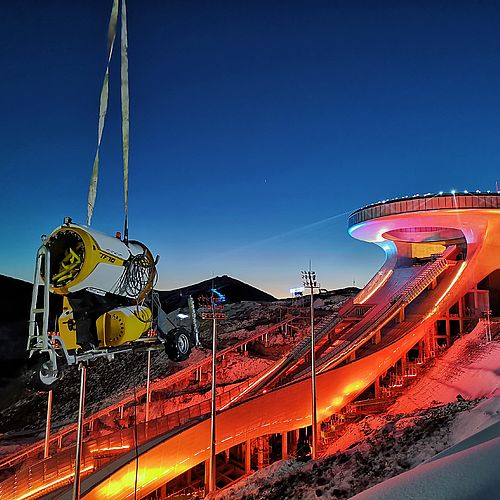 Gelber TechnoAlpin TF10 Schneeerzeuger an Kran beim Big Air Shougang Olympiastadion Peking in der Dämmerung