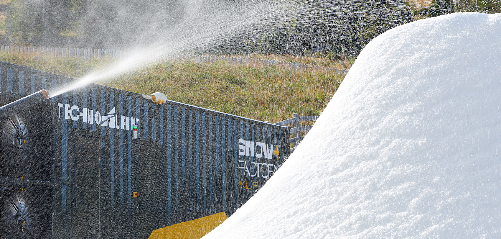 TechnoAlpin SnowFactory container producing snow as a large white pile on green meadow