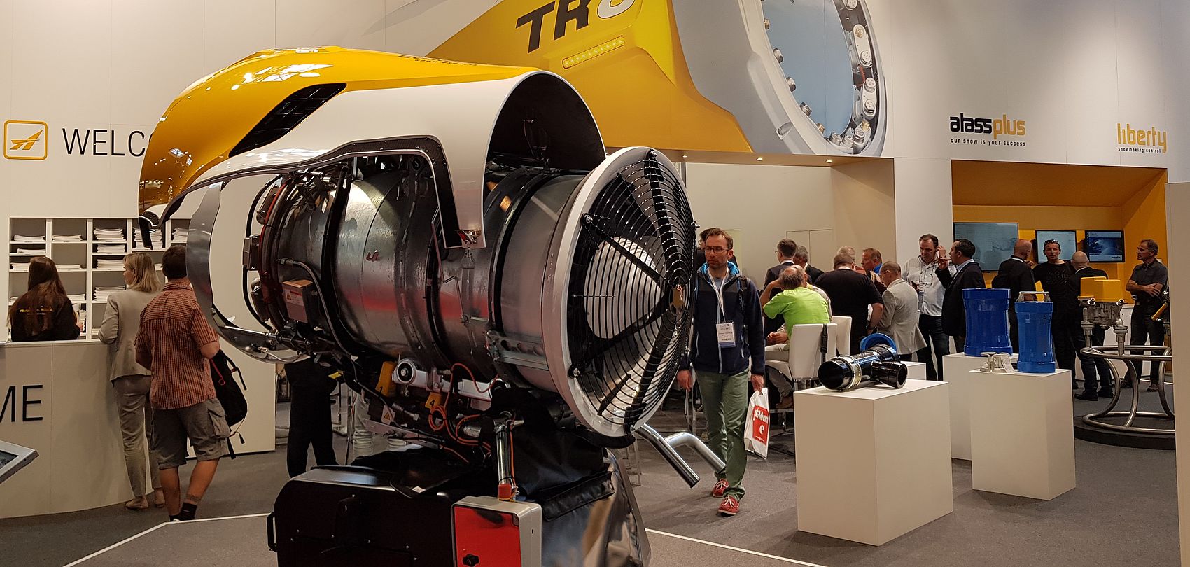 TechnoAlpin trade show stand with cross-sectioned TR8 snow generator and visitors in background.