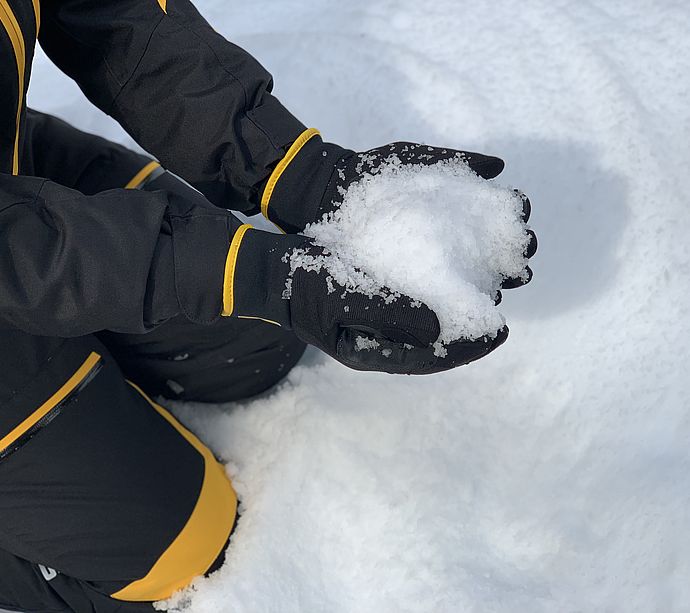 Hände in Skihandschuhen halten frisch produzierten Schnee der SNOW FACTORY