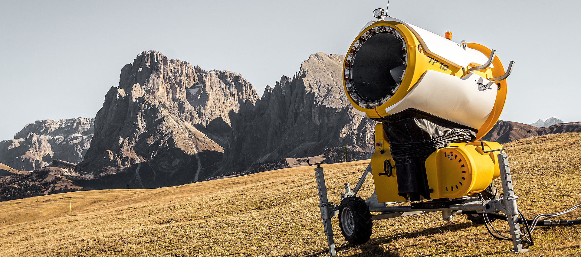 Canon à neige mobile TechnoAlpin TF10 sur roues positionné sur prairie dorée avec les pics dramatiques des Dolomites de l'Alpe di Siusi en arrière-plan