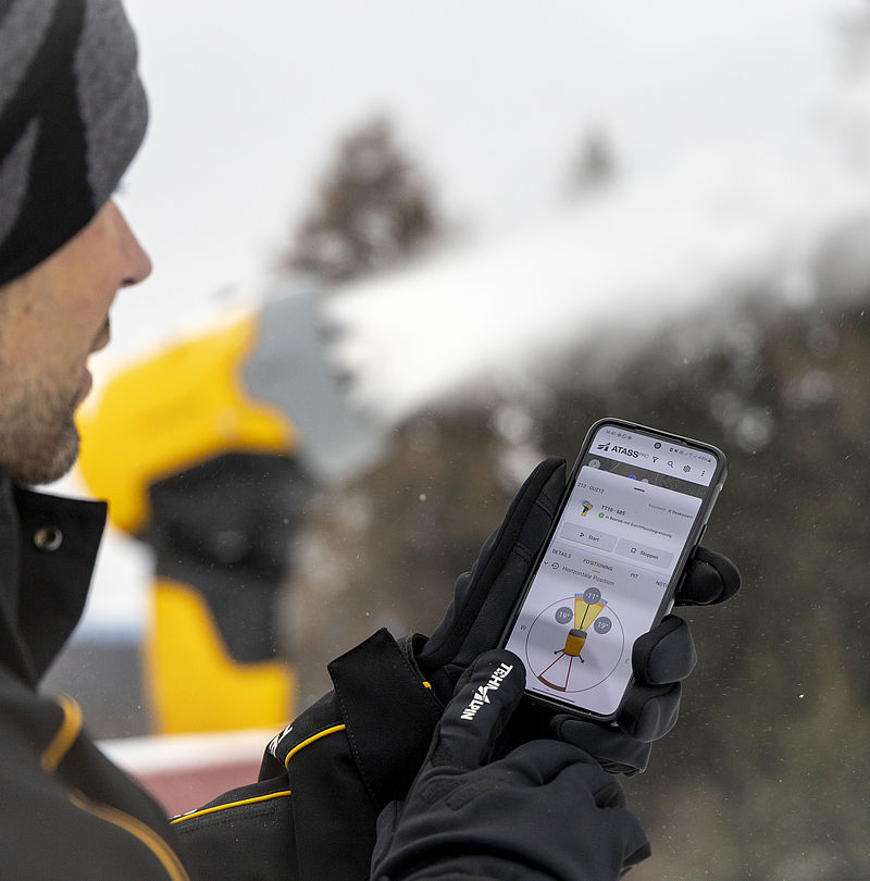Man with hat uses ATASS app on smartphone with gloves in front of snowy landscape