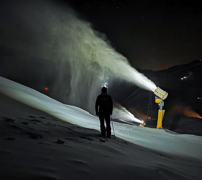 Nighttime snowmaking with person in front of illuminated snow cannon