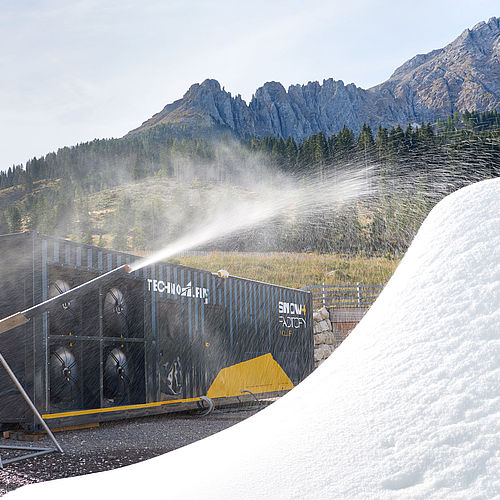SnowFactory Polar Container bläst Schnee auf weißen Haufen vor felsiger Bergkulisse der Dolomiten