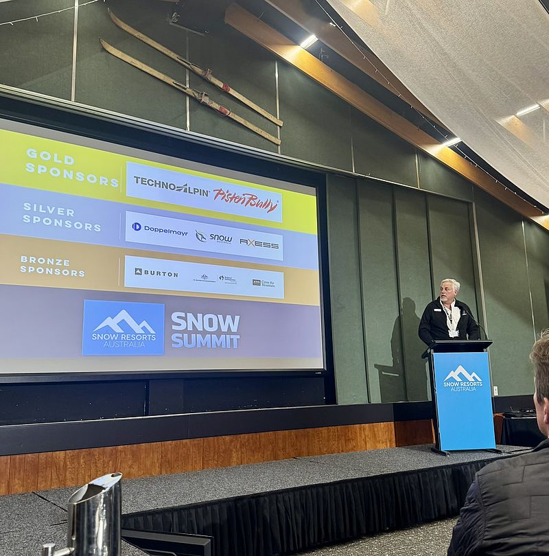 Redner am Pult beim Snow Summit Australia vor Sponsoren-Leinwand mit TechnoAlpin Logo