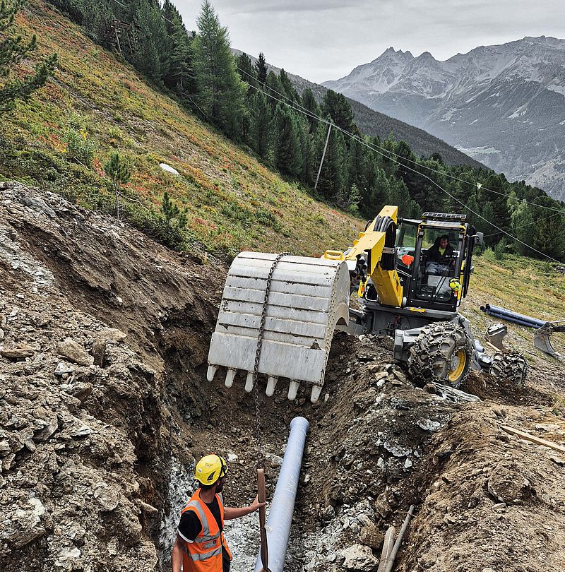 Operai posano tubazione innevamento in trincea sul fianco della montagna con escavatore
