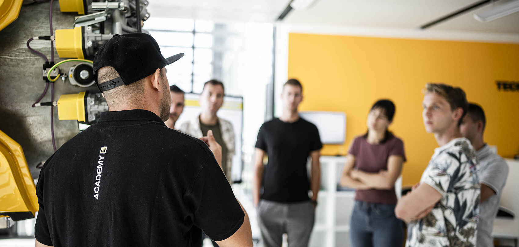 TechnoAlpin Academy Schulung mit Trainer vor gelber Schneekanone und Teilnehmergruppe