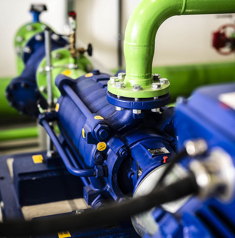 Detailaufnahme blauer Hochdruckpumpen mit grünen Rohrleitungen in einer Beschneiungspumpstation