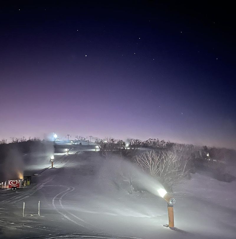 Gelbe Propellermaschine erzeugt Schnee in der Dämmerung unter sternenklarem violettem Himmel