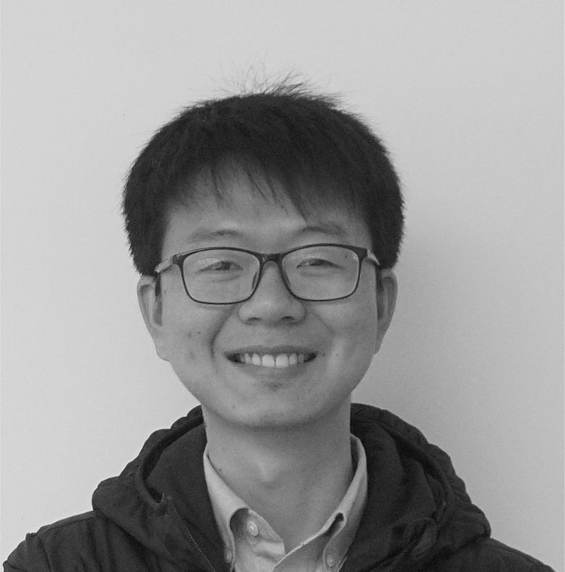 Tom Zhao, TechnoAlpin Mitarbeiter, Schwarz-Weiß-Portrait mit Brille, lächelnd in dunkler Daunenjacke vor hellem Studiohintergrund