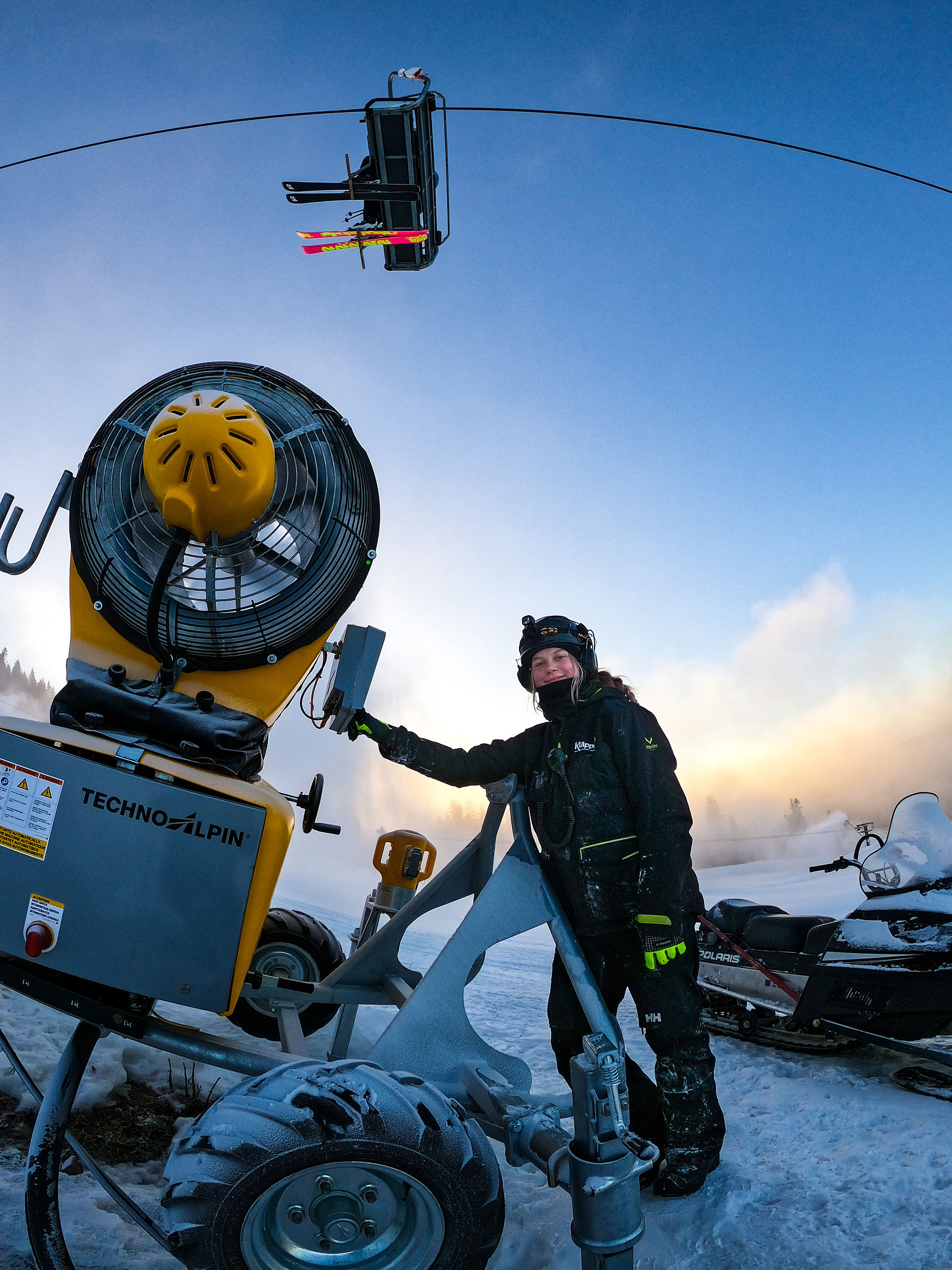 Person in winter clothing operating TechnoAlpin snow cannon at ski resort at dusk