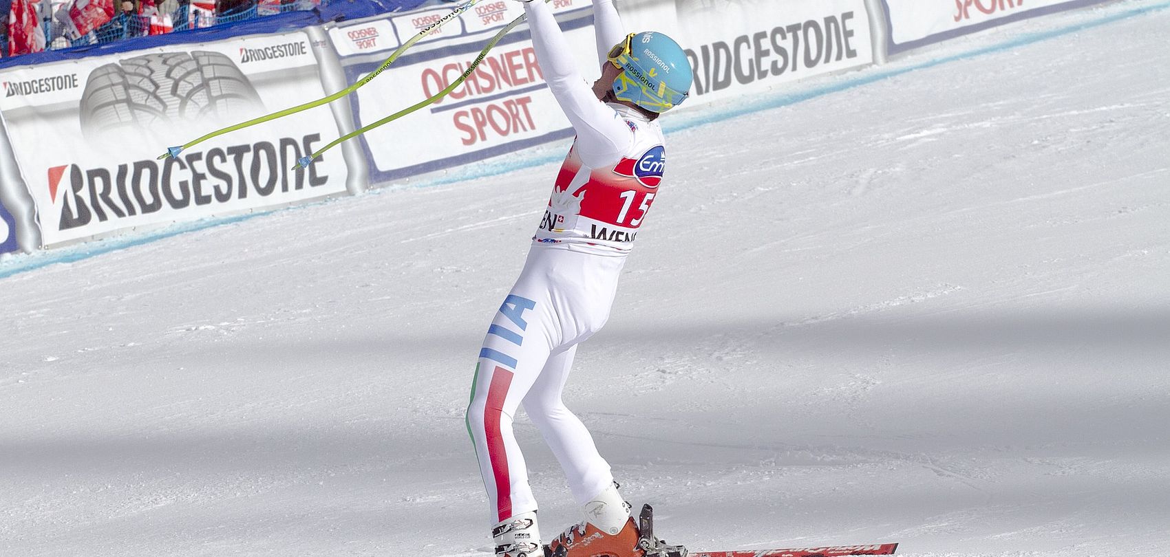 Sciatore da competizione esulta con le braccia alzate nell'area d'arrivo davanti alla tribuna a Wengen
