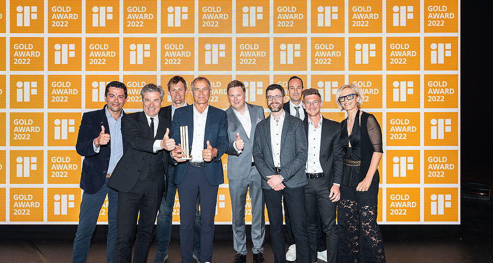 Gruppo TechnoAlpin di nove persone con trofeo davanti a parete logo iF Gold Award 2022.