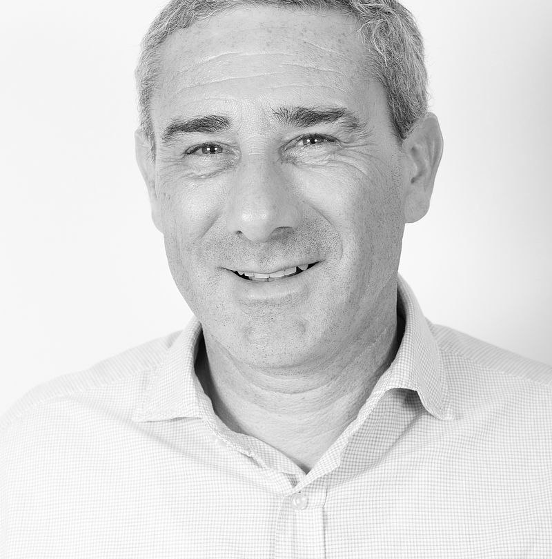 Michel Blanchot, TechnoAlpin Mitarbeiter, Schwarz-Weiß-Portrait mit grauem Kurzhaar und breitem Lächeln in hellem Hemd vor weißem Hintergrund