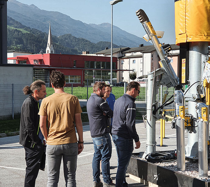 Partecipanti al roadshow esaminano tecnologia della serie TL con chiesa e montagne sullo sfondo
