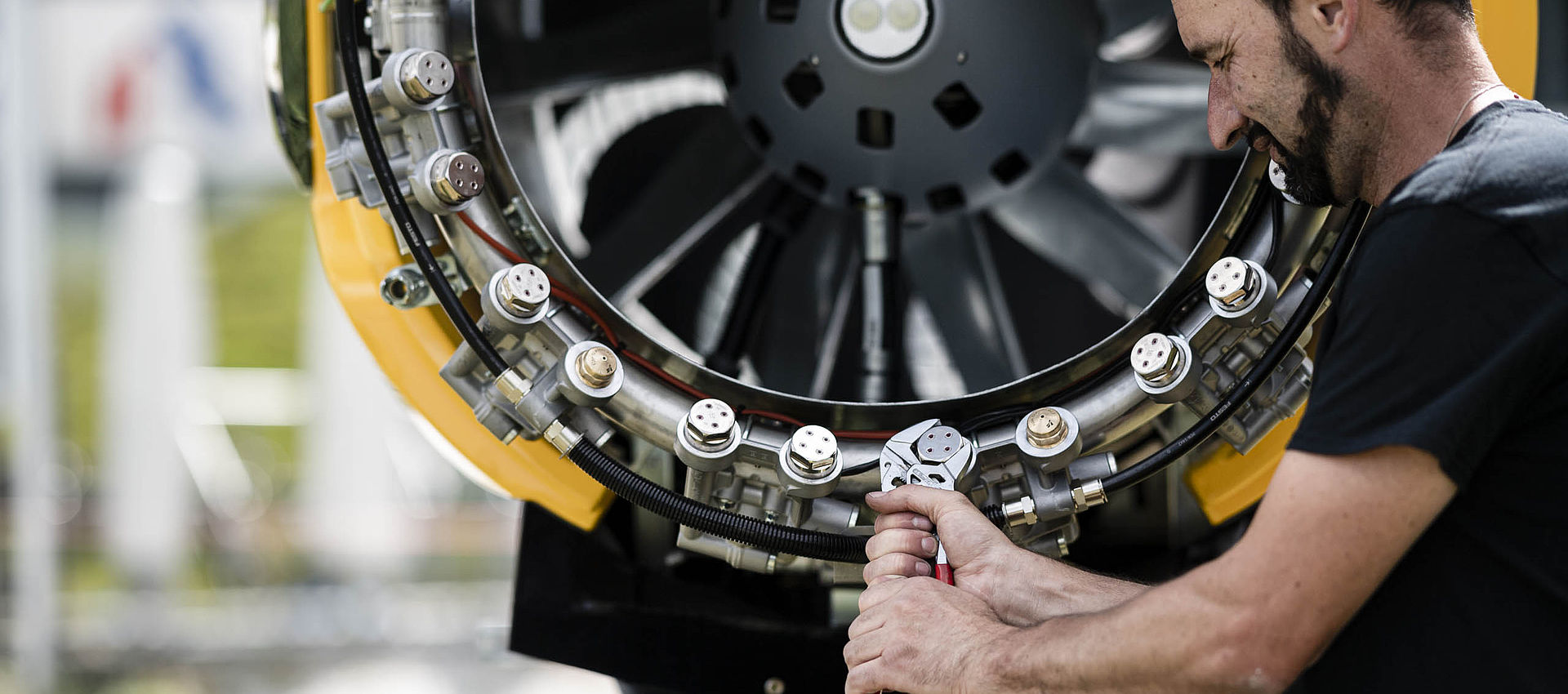 Primo piano di tecnico TechnoAlpin che lavora con pinze sull'anello ugelli di un cannone da neve giallo durante manutenzione o montaggio