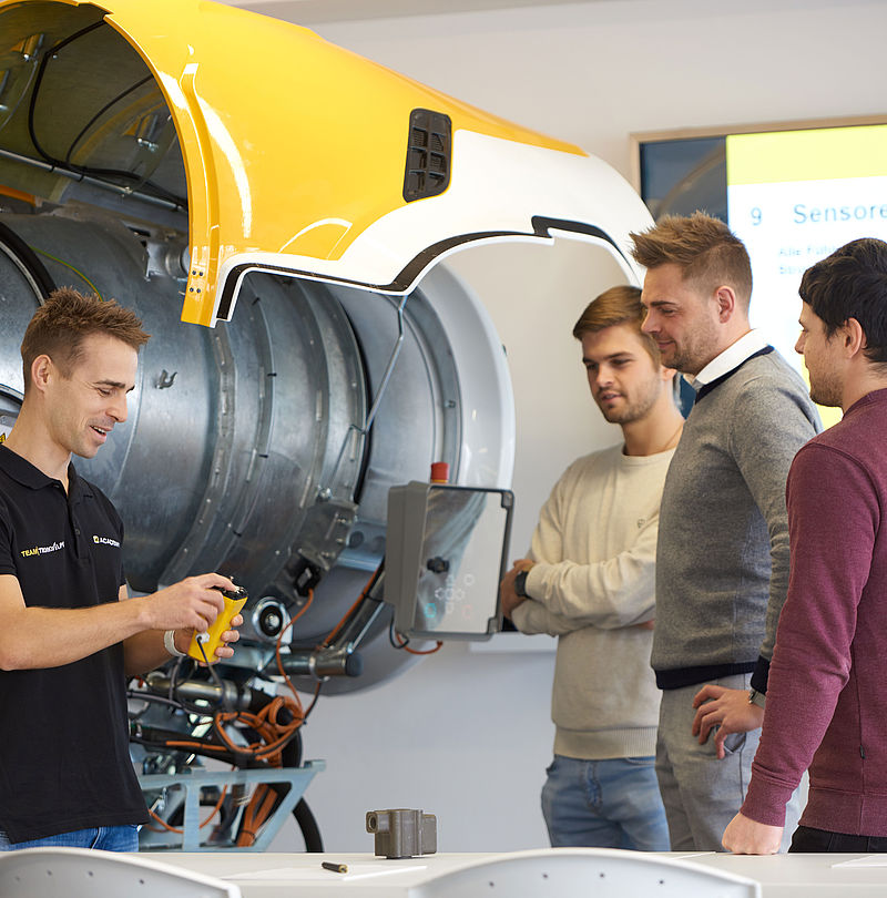 Academy trainer explaining structure of opened yellow propeller snow gun to three participants.