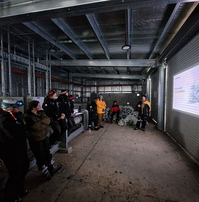 Group in ski clothing during presentation in industrial hall with projection screen
