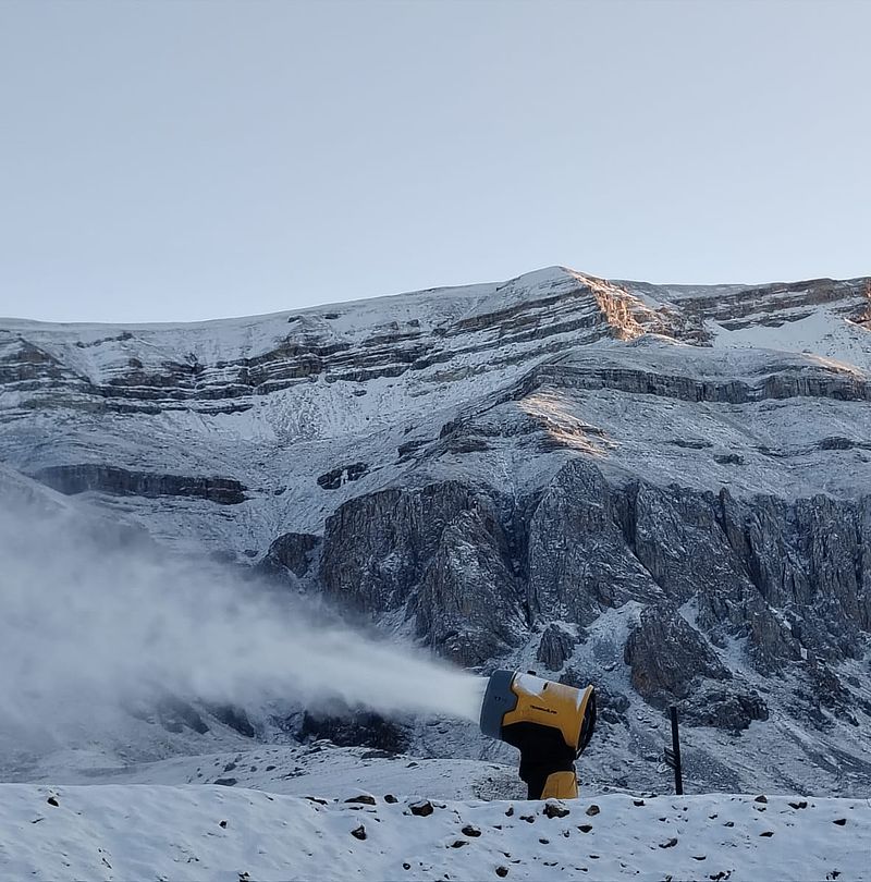 Gelber TechnoAlpin Schneeerzeuger produziert Schnee vor felsigem Bergmassiv