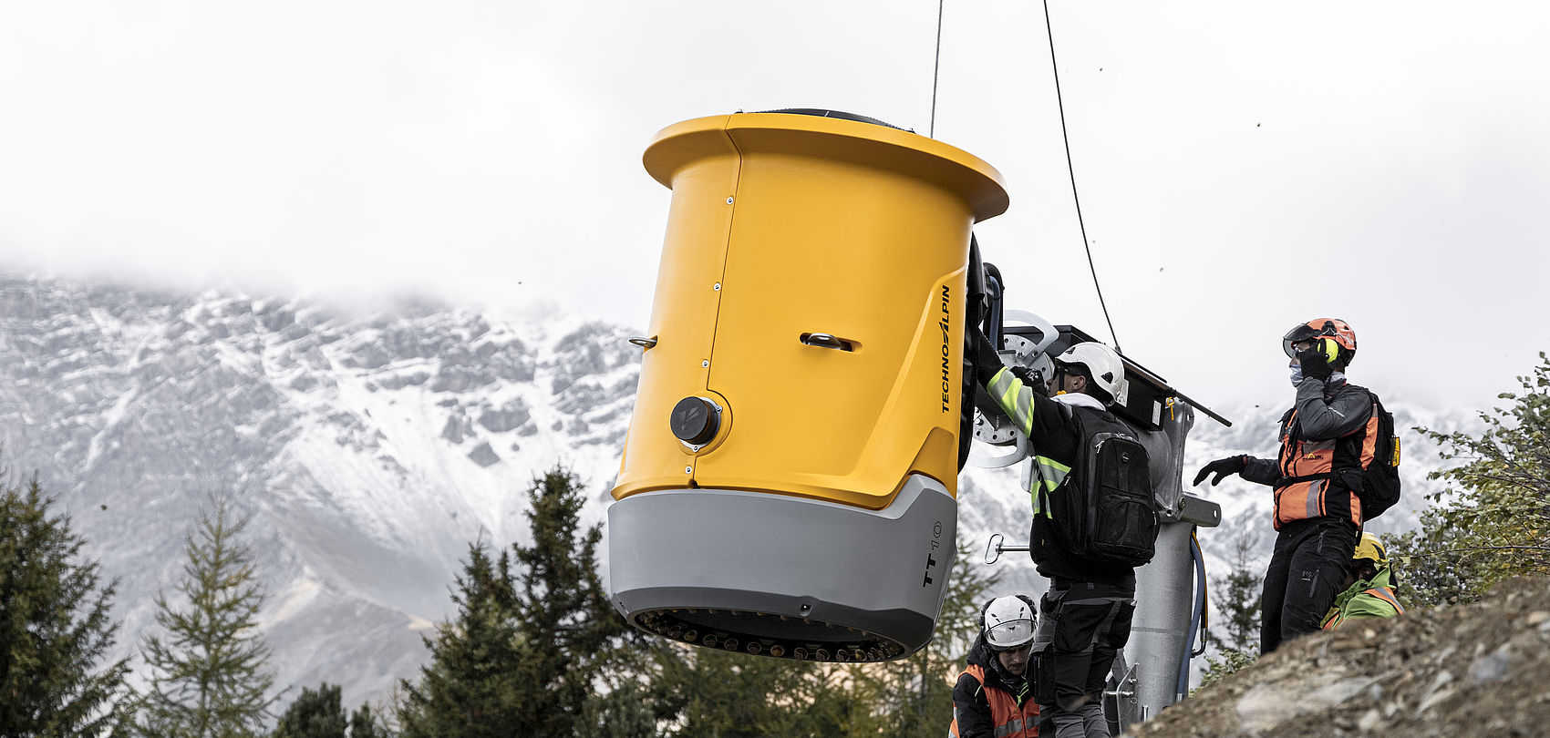 Montaggio cannone sparaneve TT giallo con gru sul fianco della montagna con monti innevati