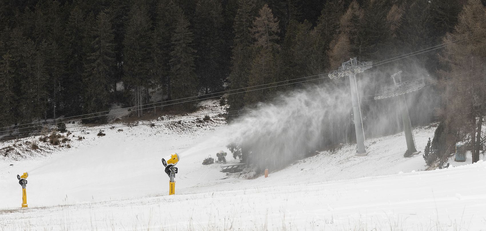 Canon à neige produit de la neige sur piste avec télésiège et forêt en arrière-plan