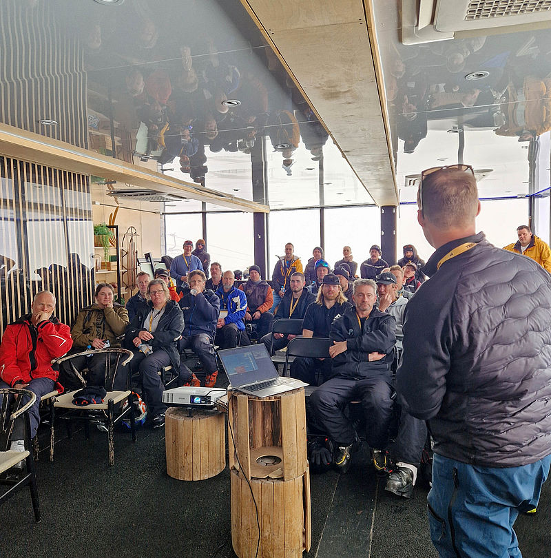 Lecture in front of seated audience in room with laptop and projector on wooden log