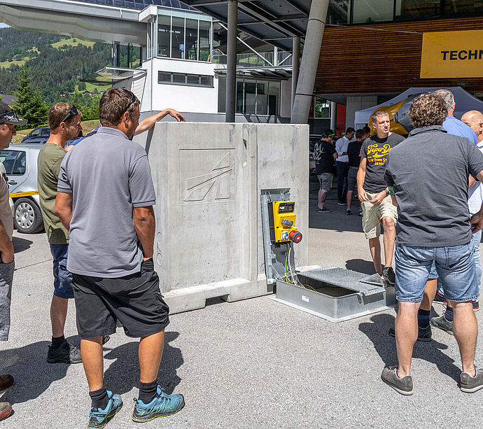 Group examining precast concrete element with TechnoAlpin logo and electrical connection panel.