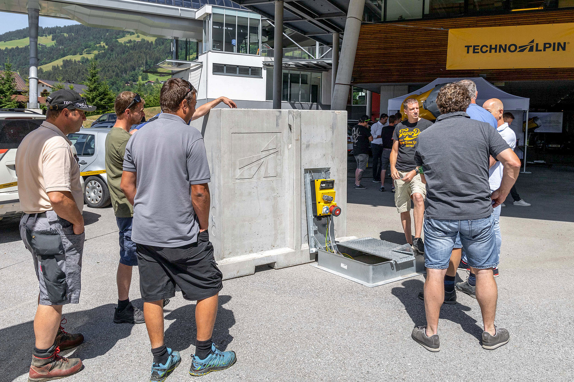Group examining precast concrete element with TechnoAlpin logo and electrical connection panel.